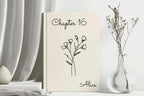 A cream-colored hardcover book standing upright on a tabletop, printed with the text 'Chapter 16' and 'Alice' in black script, with a simple black floral line drawing in the center. The book is styled in a bright, minimalist room setting with draped white fabric, a small white vase, and dried stems in a clear glass vase.
