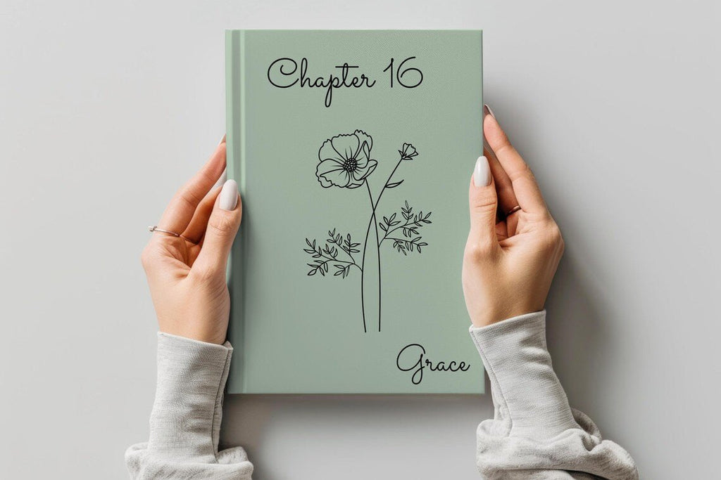 A person holds a sage green hardcover journal with 'Chapter 16' and the name 'Grace' printed on the cover, featuring a minimalist black line drawing of a flower. The person is wearing a light gray long-sleeve top, and the background is a clean, neutral gray wall.