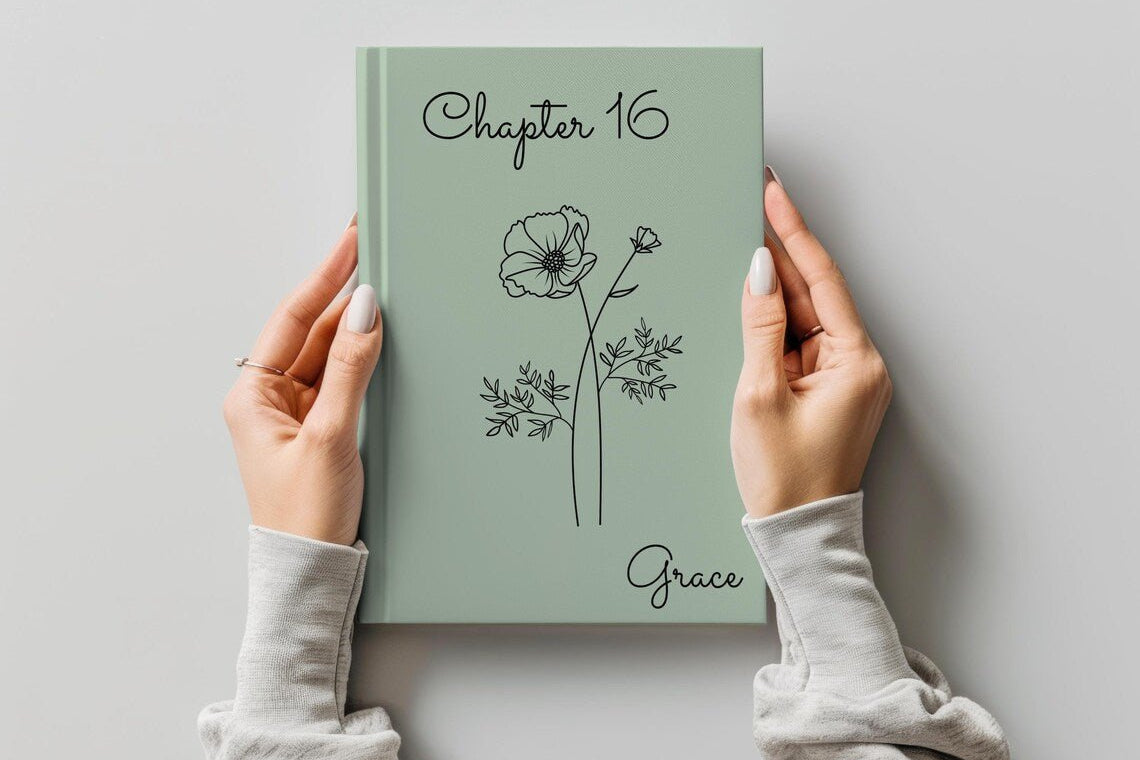 A person holds a sage green hardcover journal with 'Chapter 16' and the name 'Grace' printed on the cover, featuring a minimalist black line drawing of a flower. The person is wearing a light gray long-sleeve top, and the background is a clean, neutral gray wall.