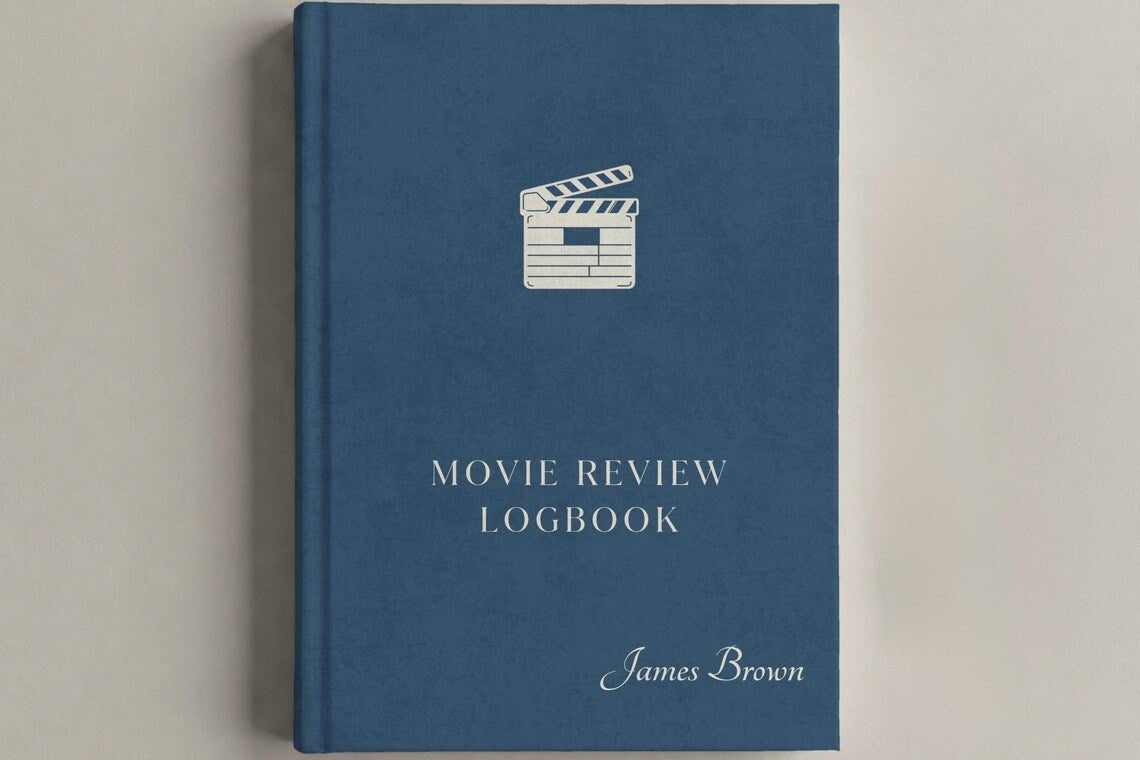 A hardcover movie review logbook in slate blue with a white clapperboard icon and white text, including the name James Brown, shown on a neutral light gray background.