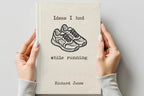 A person holds a cream-colored hardcover notebook with a black typewriter-style illustration of running shoes and the text 'Ideas I had while running' and 'Richard Jones' on the cover, against a light gray background.